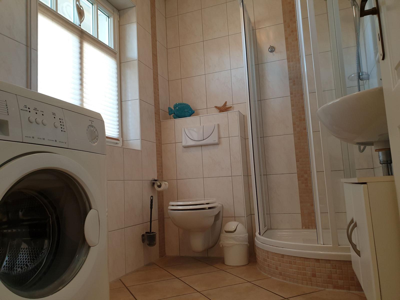 Badezimmer mit Dusche, Toilette, Waschmaschine und Waschtisch.