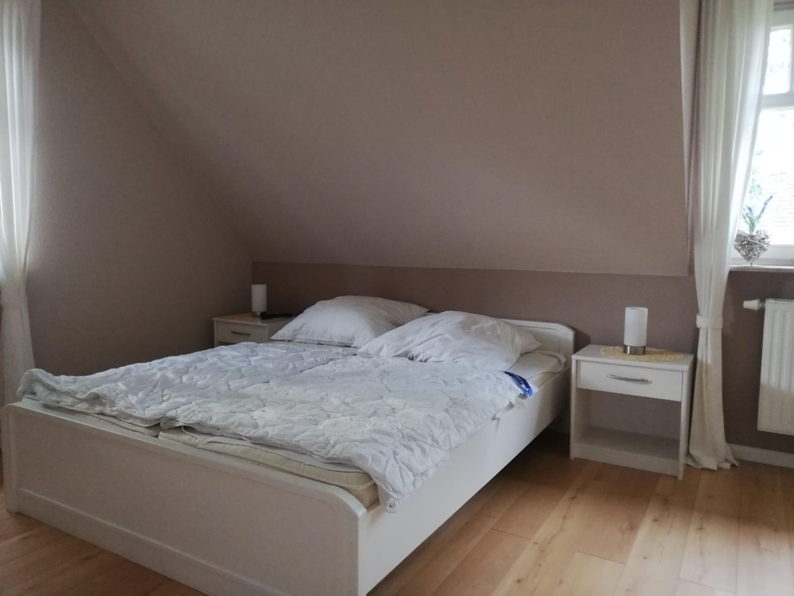 Schlafzimmer mit Dachschrägen, weißem Bett und zwei Nachttischen.