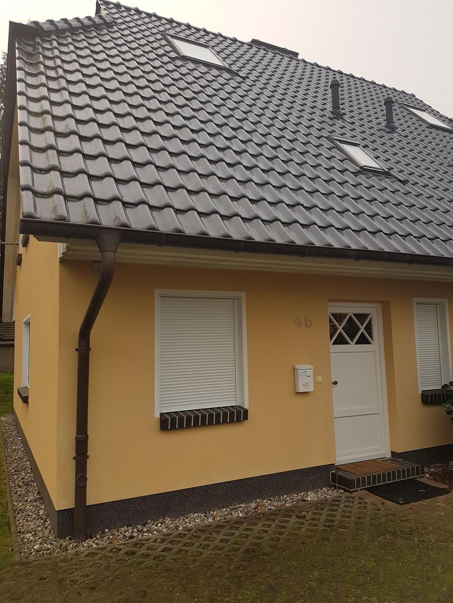 Gelbes Einfamilienhaus mit grauem Satteldach und weißer Eingangstür.