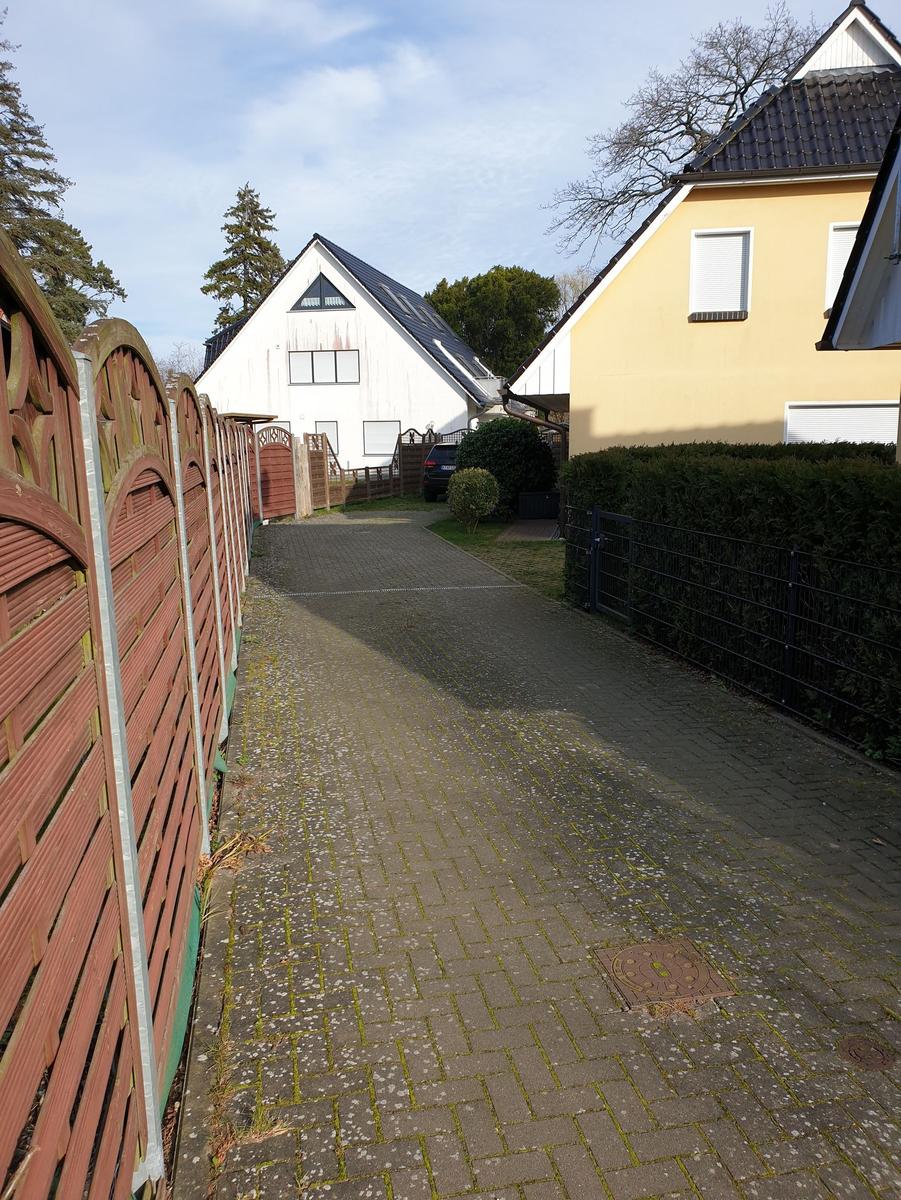 Pflasterweg zwischen zwei Häusern mit Zaun und Hecke