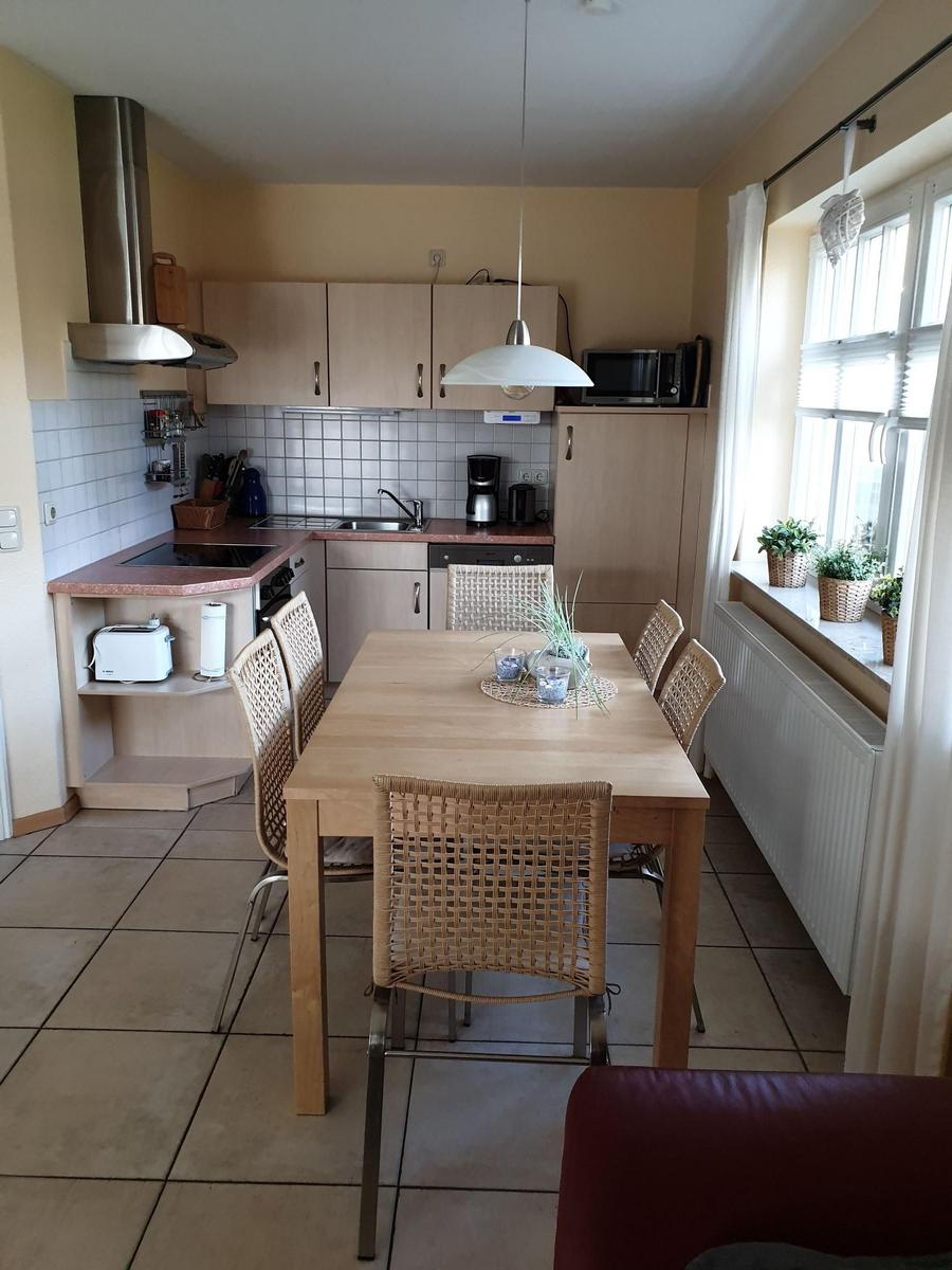 Küche mit Essbereich, Holztisch und Stühlen, Fenster mit Pflanzen.