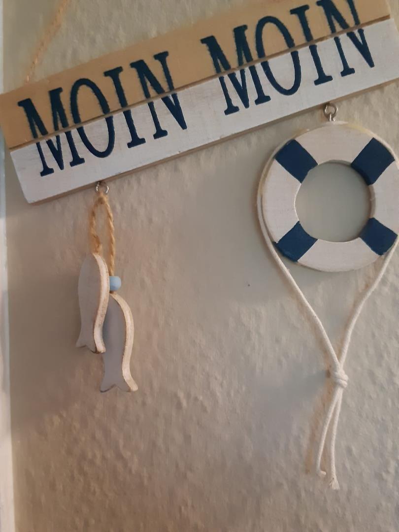 Wanddekoration mit Segelschild, Rettungsring und Fischfiguren in blau-weiß.