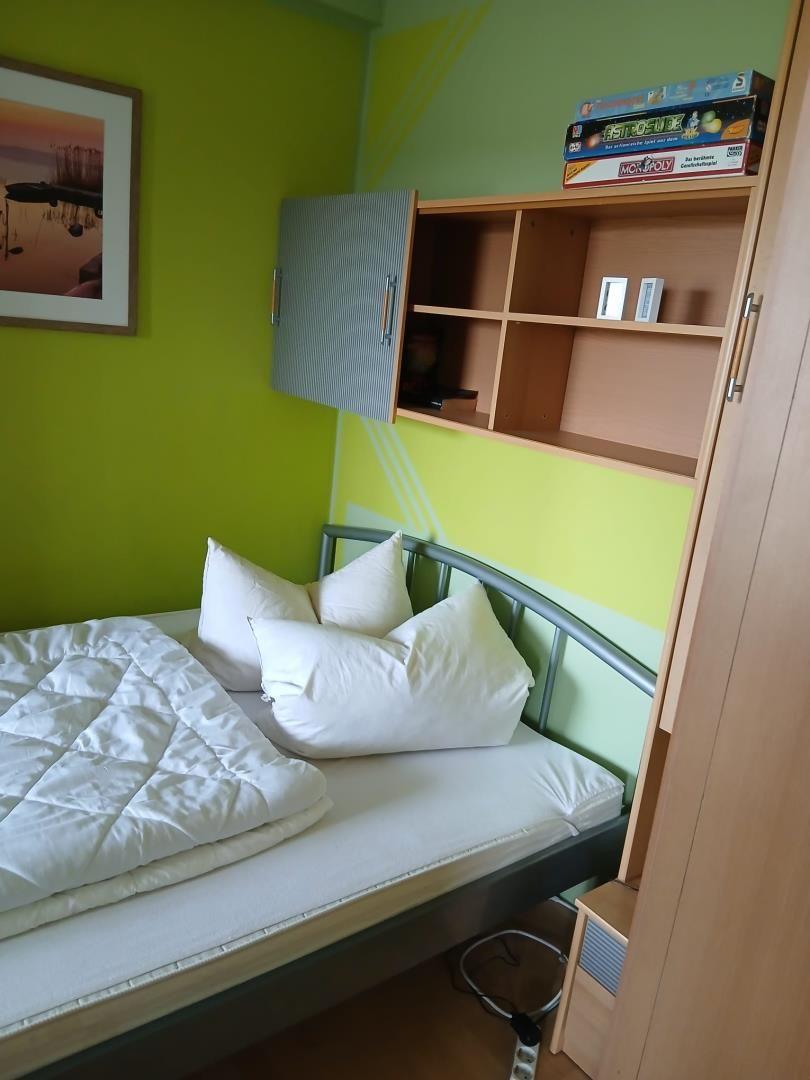 Ein Schlafzimmer mit Bett, Schrank und Regal an der Wand.