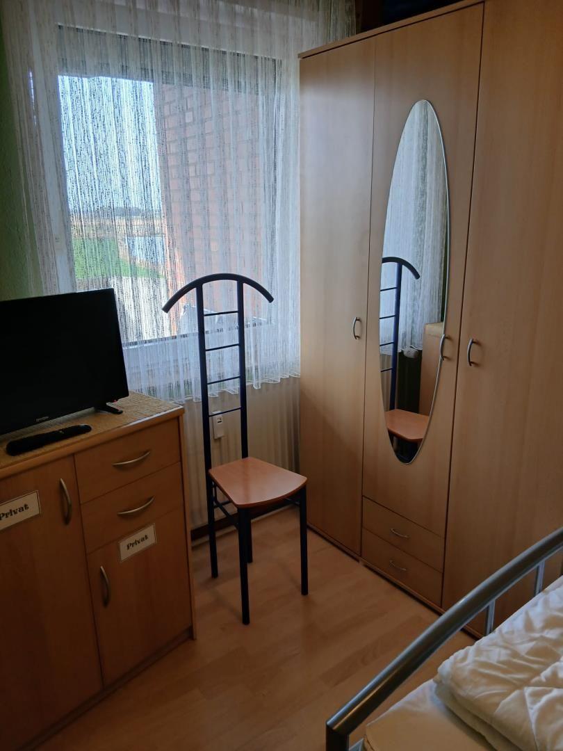 Schlafzimmer mit Kleiderschrank, Stuhl und TV-Schrank vor Fenster