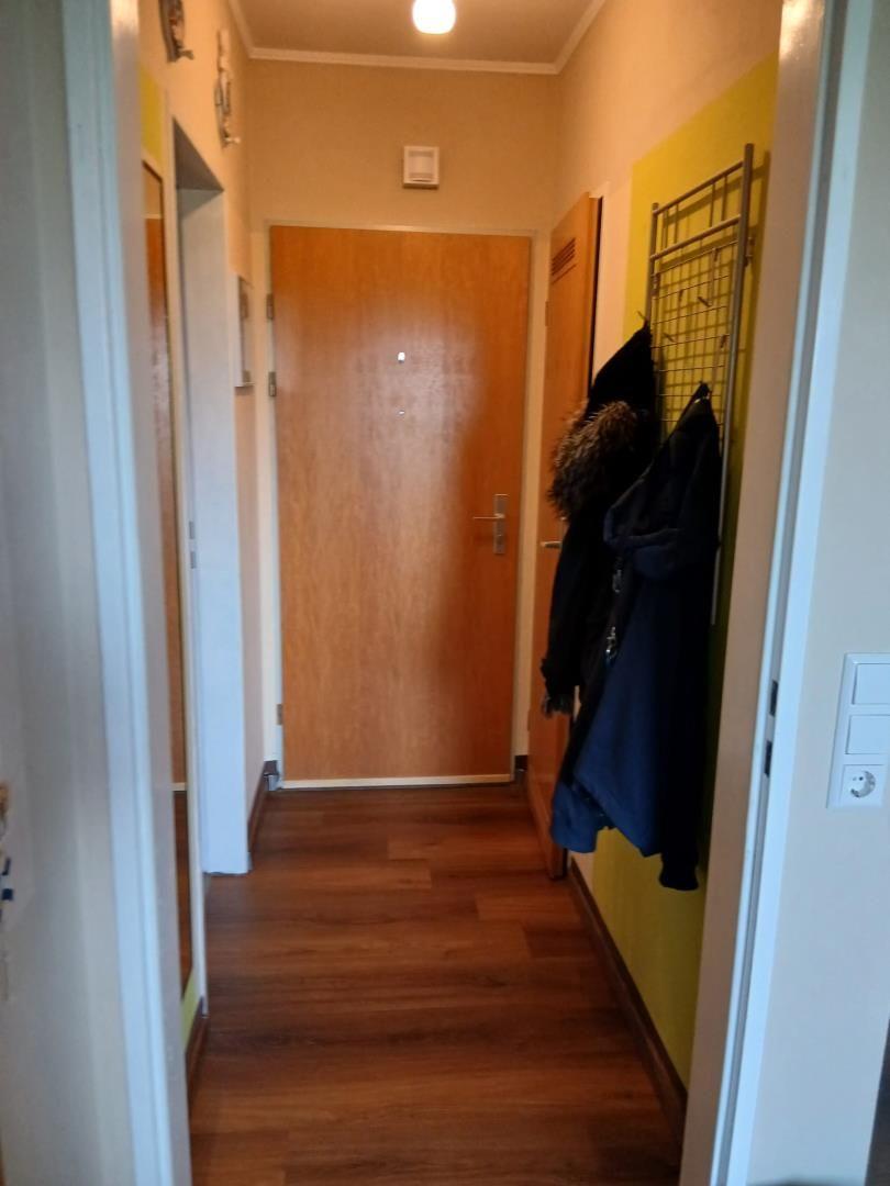 Flur mit Holzboden, gelber Wand und Garderobe mit Jacken.