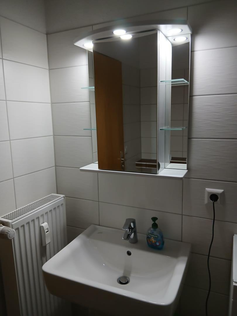 Bad mit Spiegel, Waschbecken und Heizkörper an der Wand.