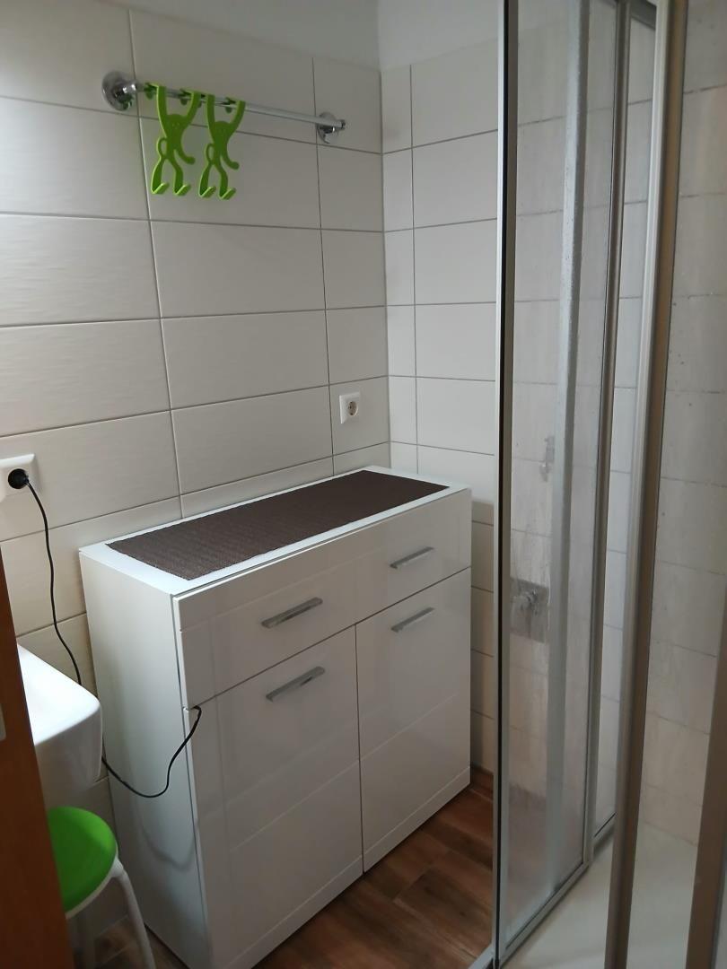 Badezimmer mit Dusche, Waschbecken und Schrank.