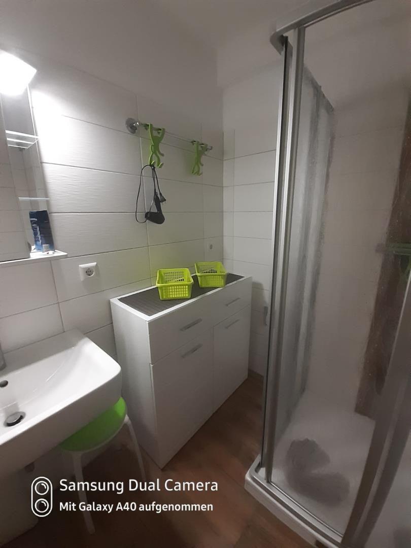 Badezimmer mit Dusche, Waschbecken und grünen Körben.