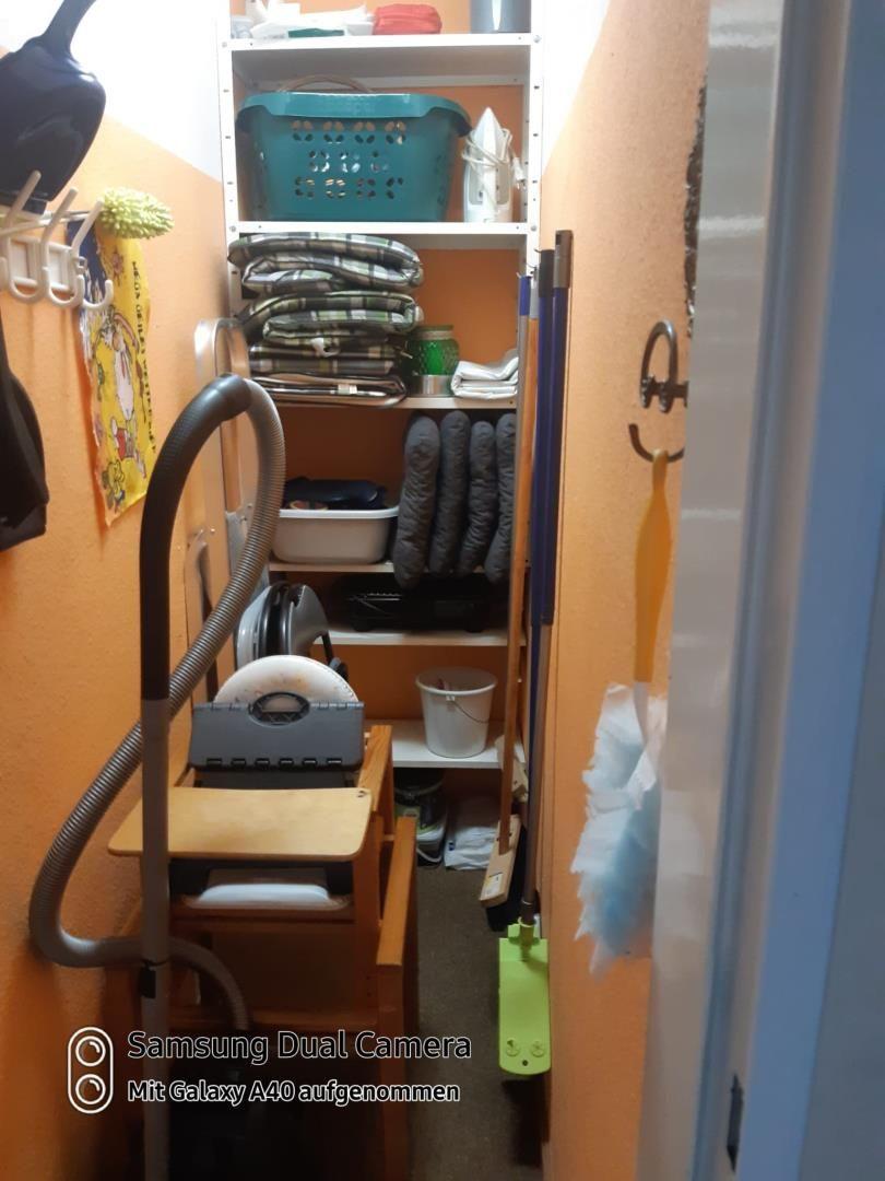 Kleiner Raum mit Schrank, Staubsauger und Reinigungsmitteln.