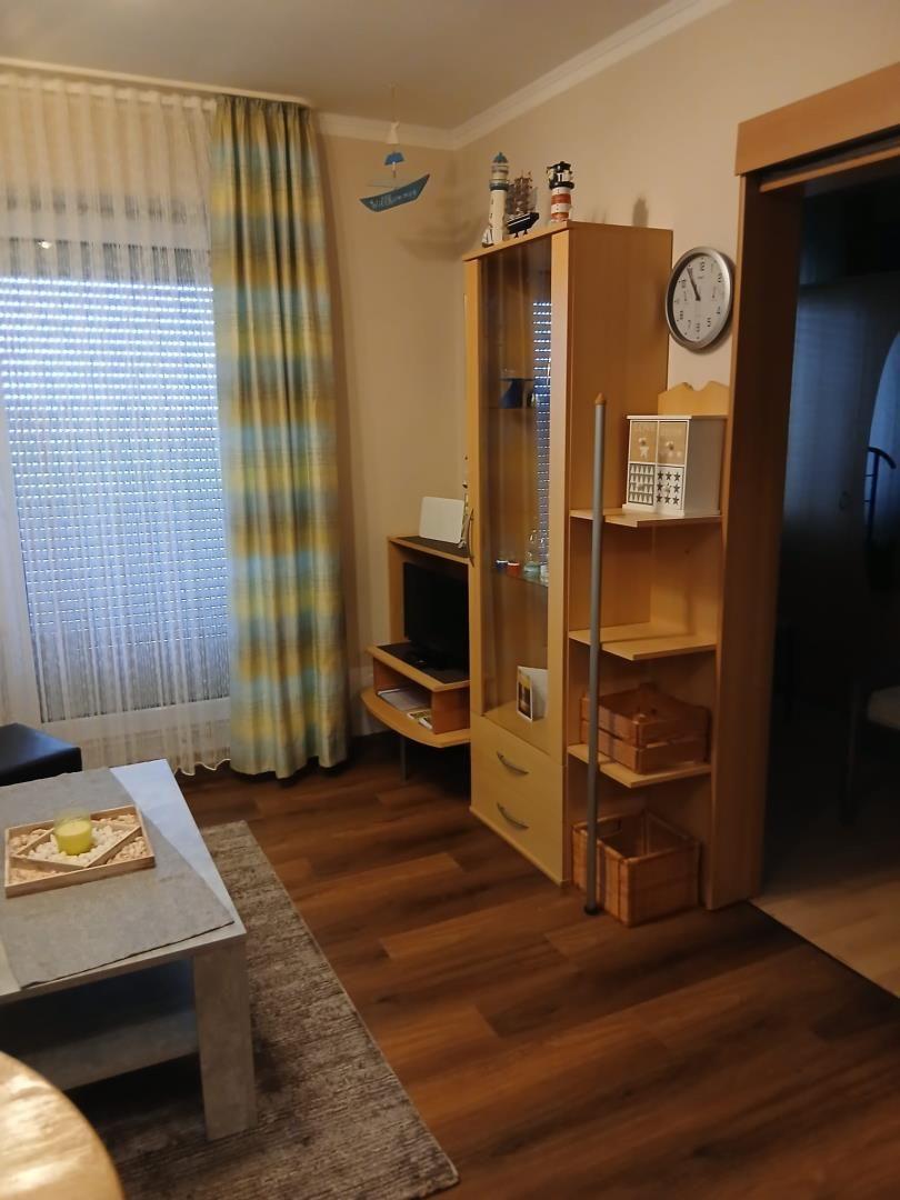 Wohnzimmer mit Holzboden, TV, Bücherregal und Fenster mit Vorhängen.