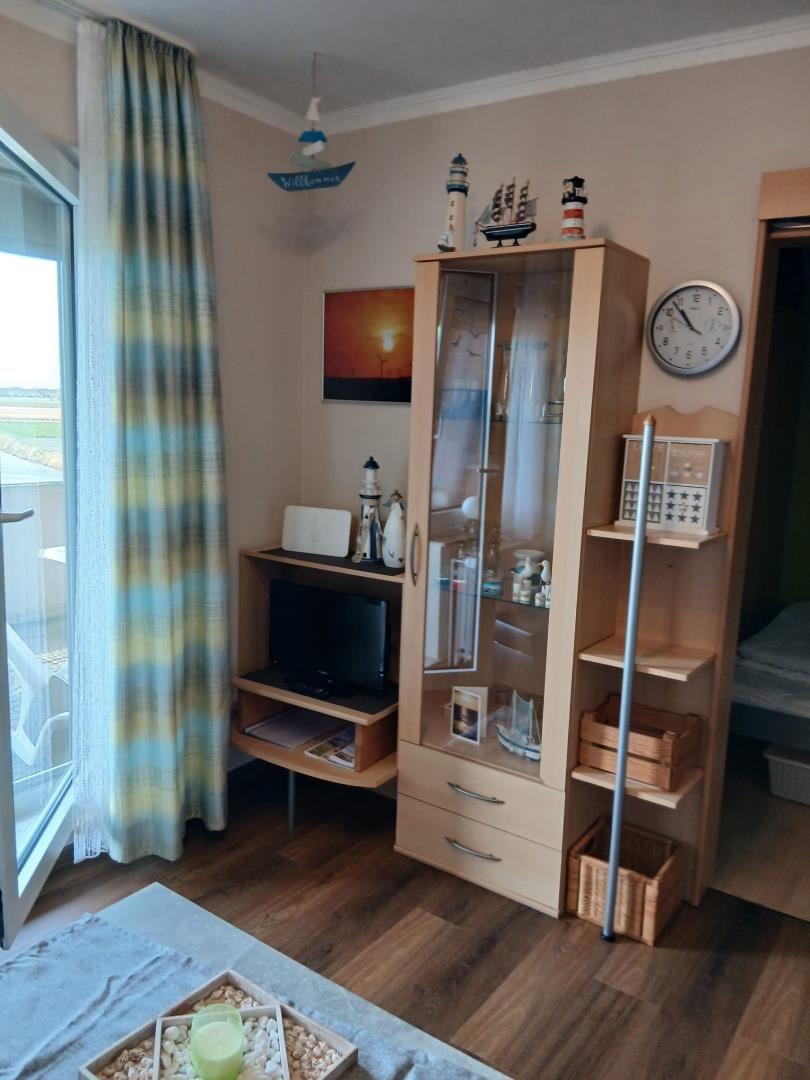 Wohnzimmer mit Fernseher, Glasvitrine und Balkonzugang.