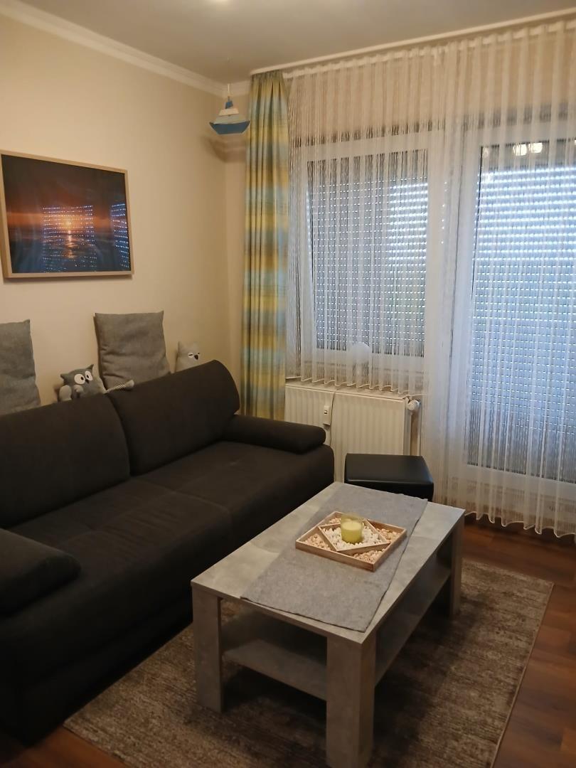 Wohnzimmer mit Sofa, Couchtisch und Fenster mit Vorhängen.