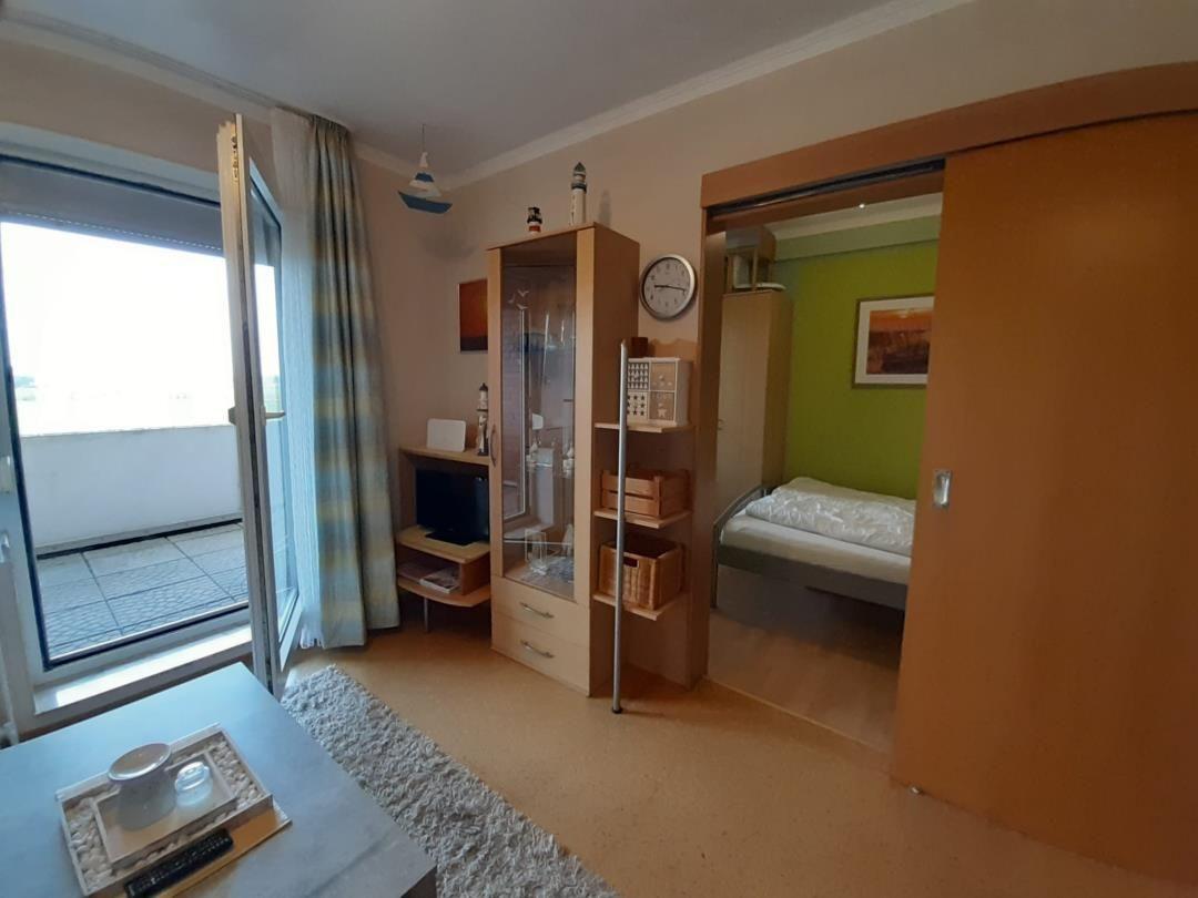 Wohnbereich mit Balkon, Schrank und Blick in Schlafzimmer.