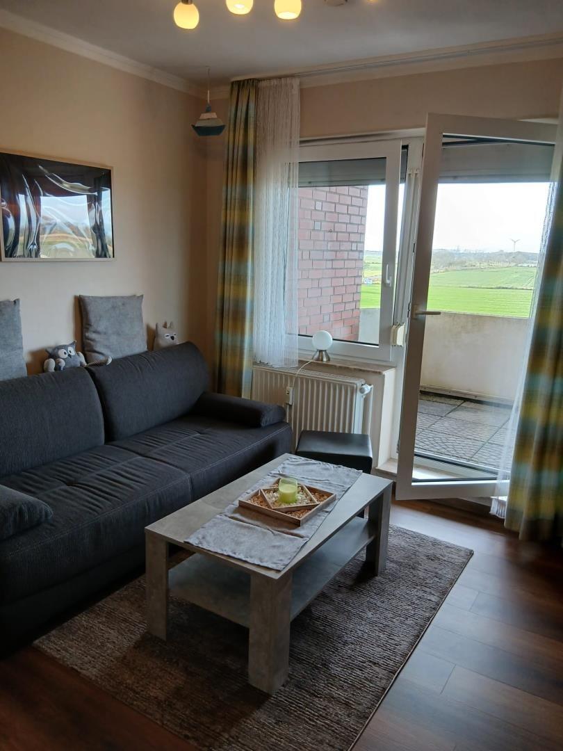 Wohnzimmer mit Sofa, Couchtisch und Balkon mit Blick auf Felder.