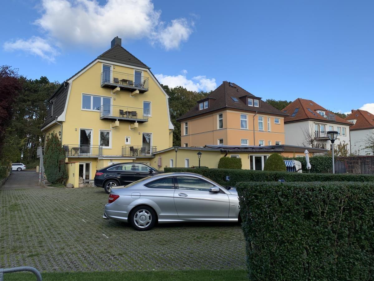 Gelbes Haus mit Balkonen und gepflastertem Hof mit parkenden Autos.