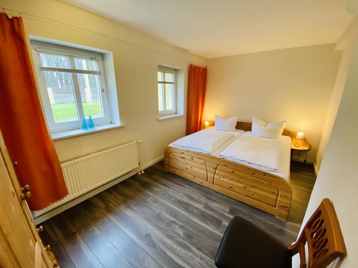 Schlafzimmer mit Doppelbett, Holzboden und Fenstern mit Vorhängen.