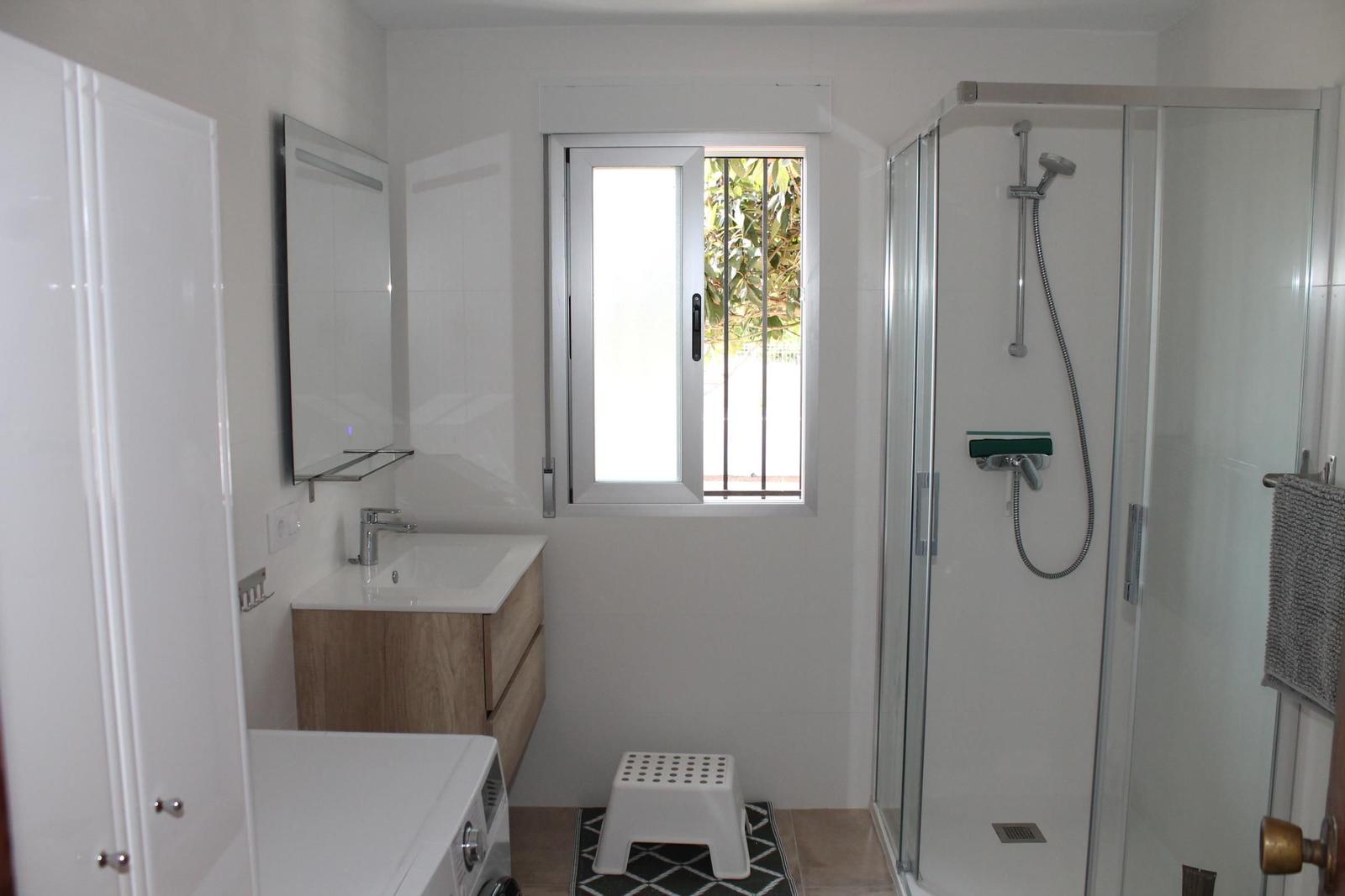 Badezimmer mit Dusche, Waschbecken und Fenster.