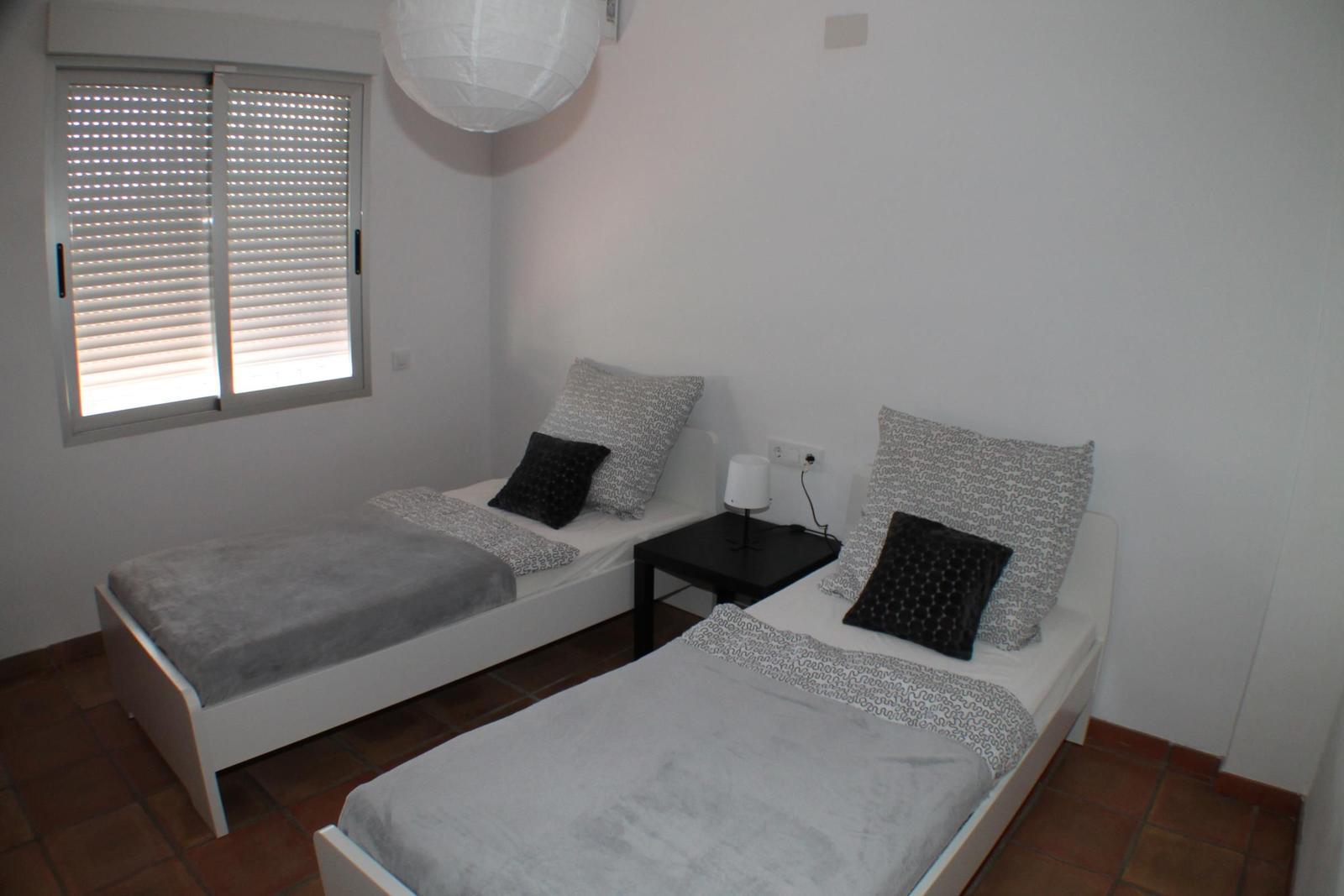 Zwei Einzelbetten mit Kissen und Decken, kleiner Nachttisch und Fenster mit Jalousien.