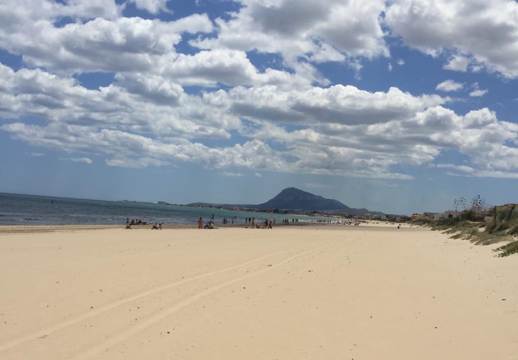 Weiterer Strand mit Sand, Meer und Berg im Hintergrund.