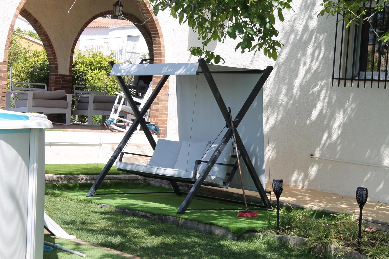 Schwinger mit Sonnenschutz im Garten neben Pool und Sitzgelegenheiten.