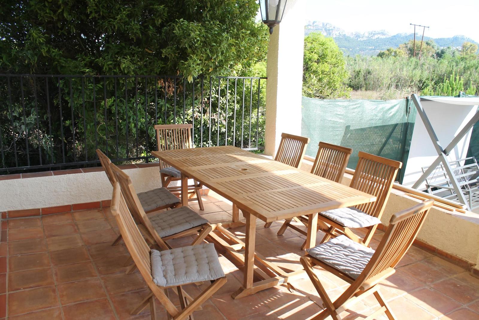 Terrasse mit Holztisch und Stühlen, Blick auf grüne Landschaft und Berge.