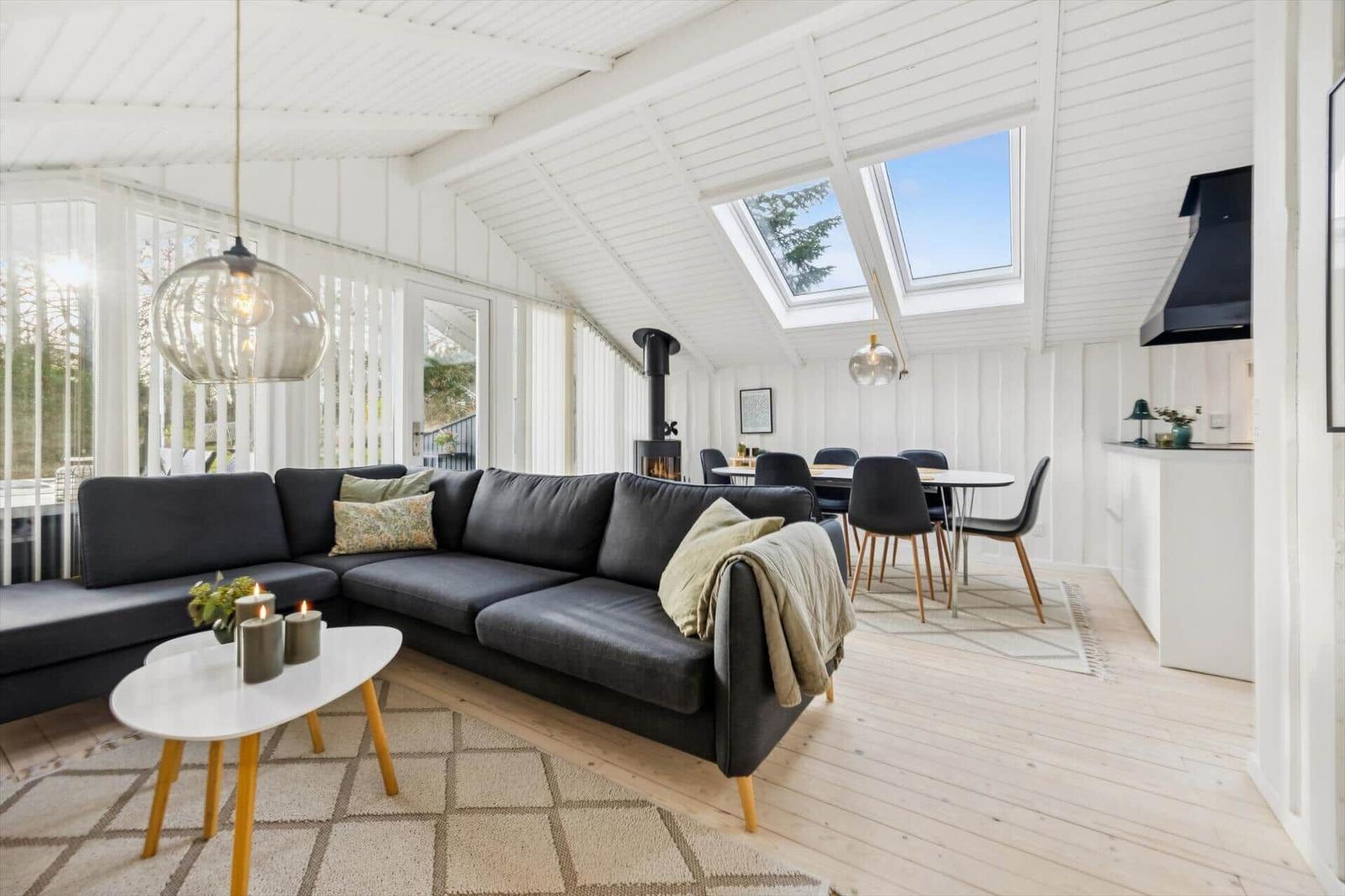 Living room with sofa bed, dining area, and skylights. Wooden floor and white walls.
