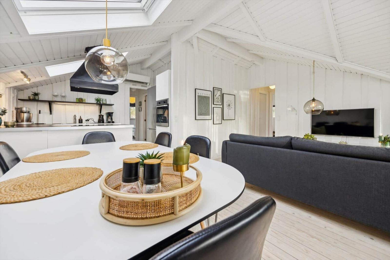 Dining area with white table and gray sofa. Kitchen and living room are connected.