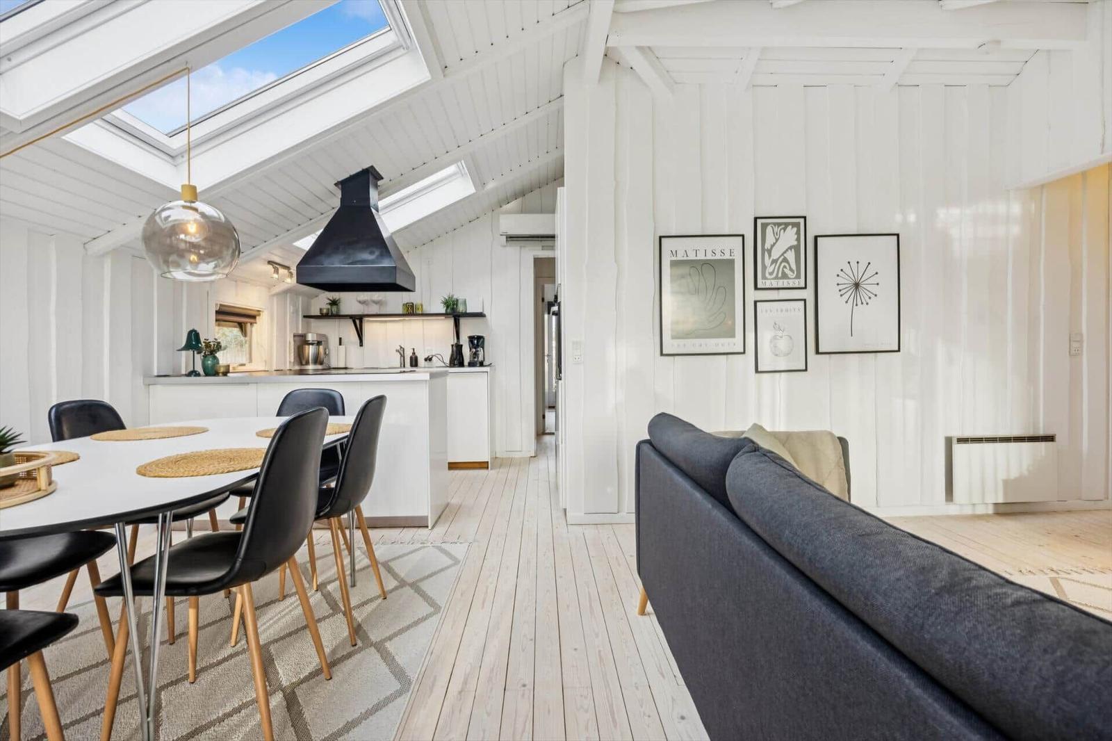 Living and dining area with kitchen under sloped ceilings and large windows.