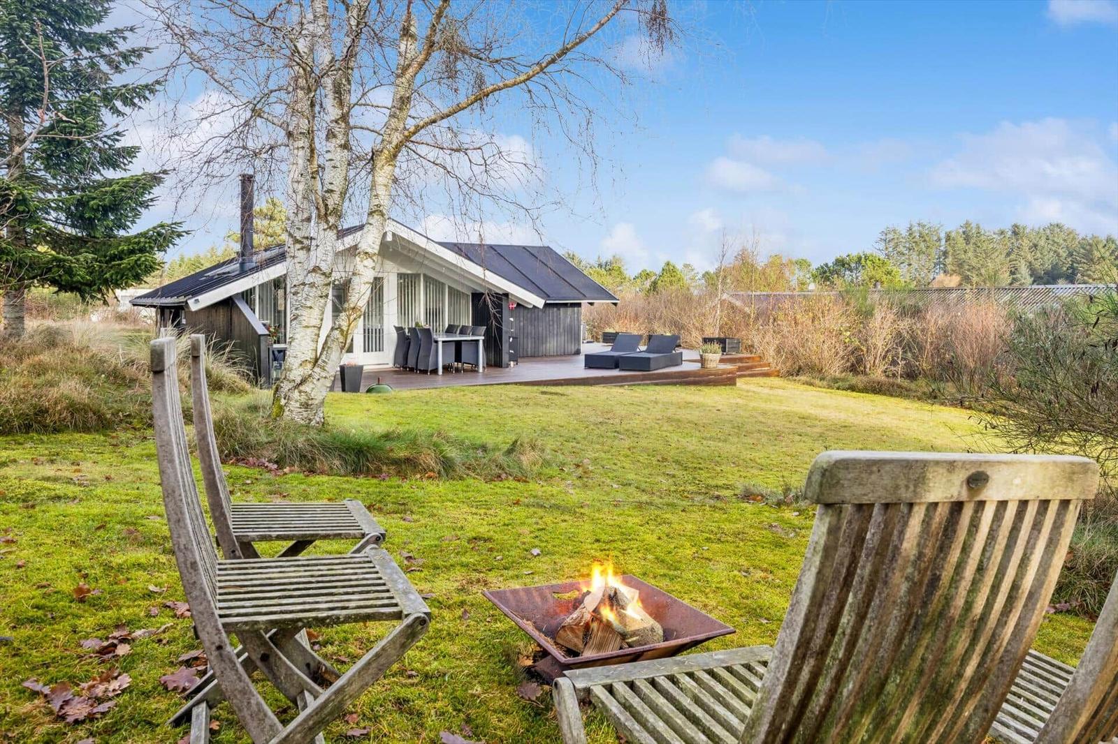 House with garden, wooden chairs, and fire pit in foreground.