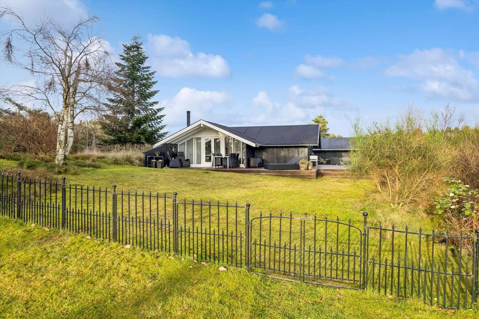 Modern house with terrace and garden. Black roofs, white window front. Surrounded by grass and trees.