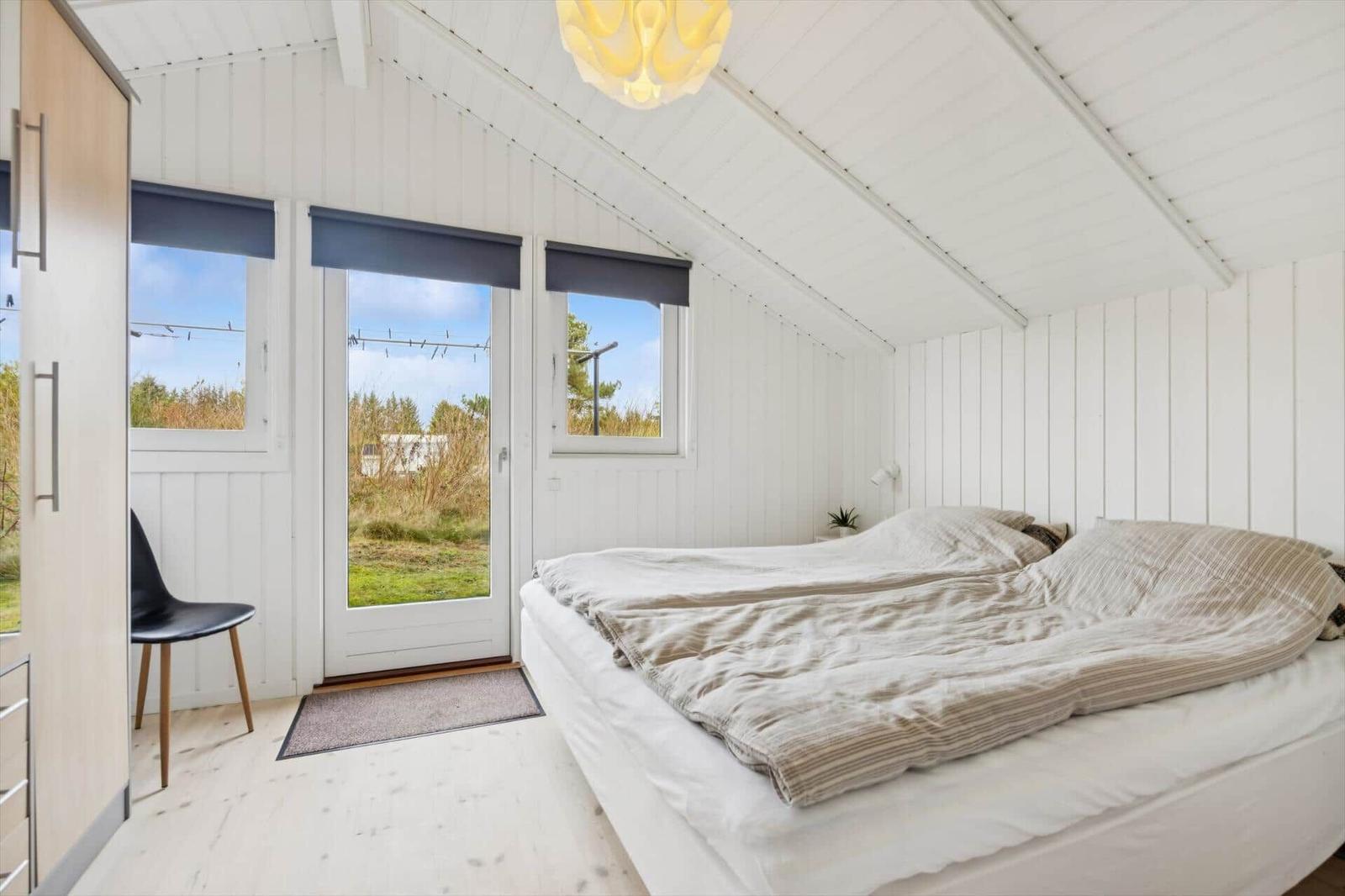 Bedroom with double bed, windows, and door to green outdoor area.