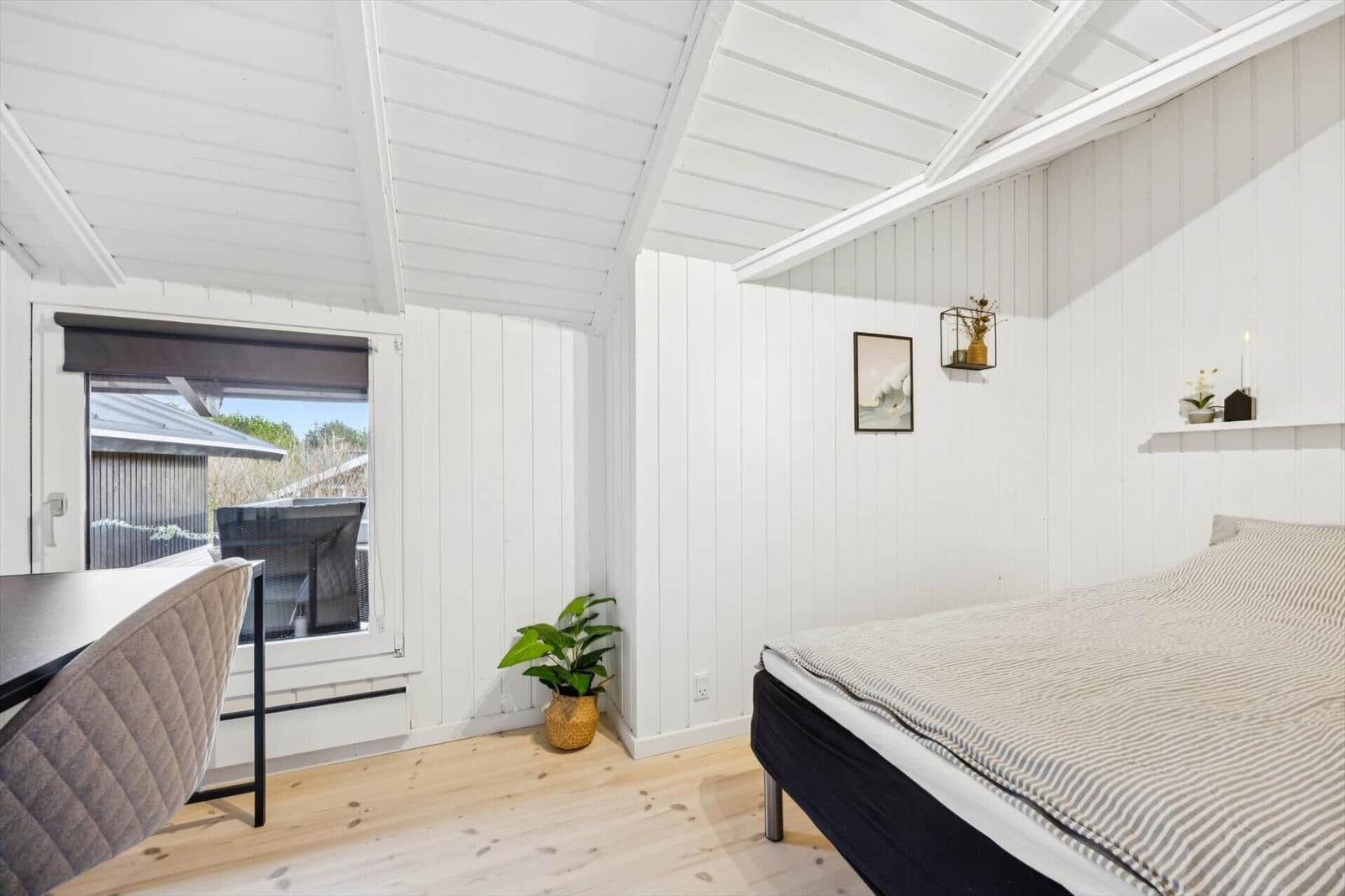 Bedroom with bed, table, plant, and window view.
