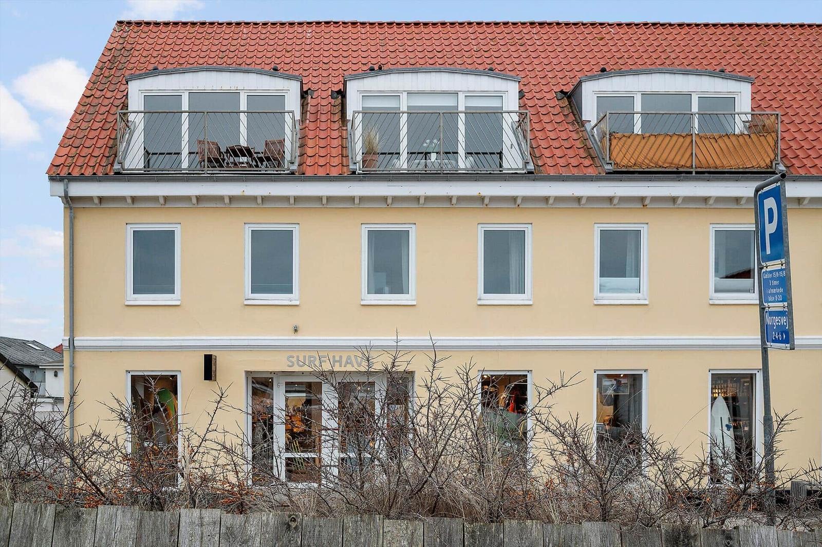 A yellow building with a red roof and three rooftop terraces with balconies.