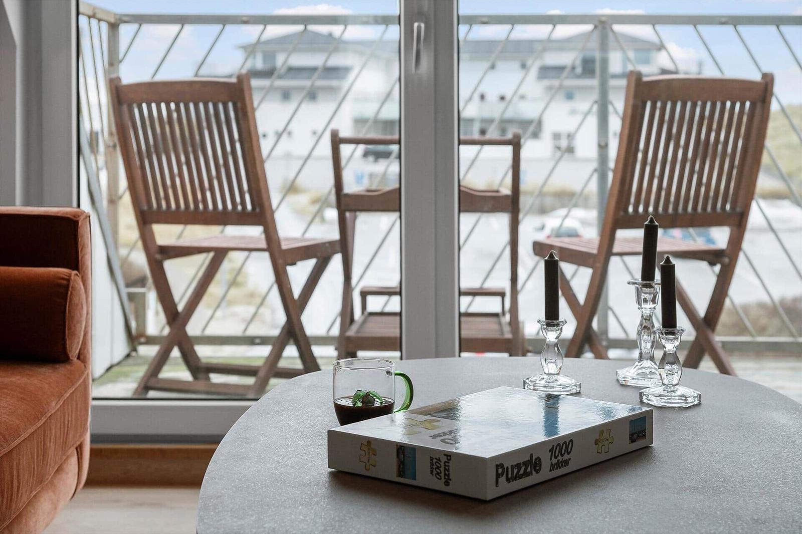 Round table with puzzle, mug, and candle holders before balcony with wooden chairs.