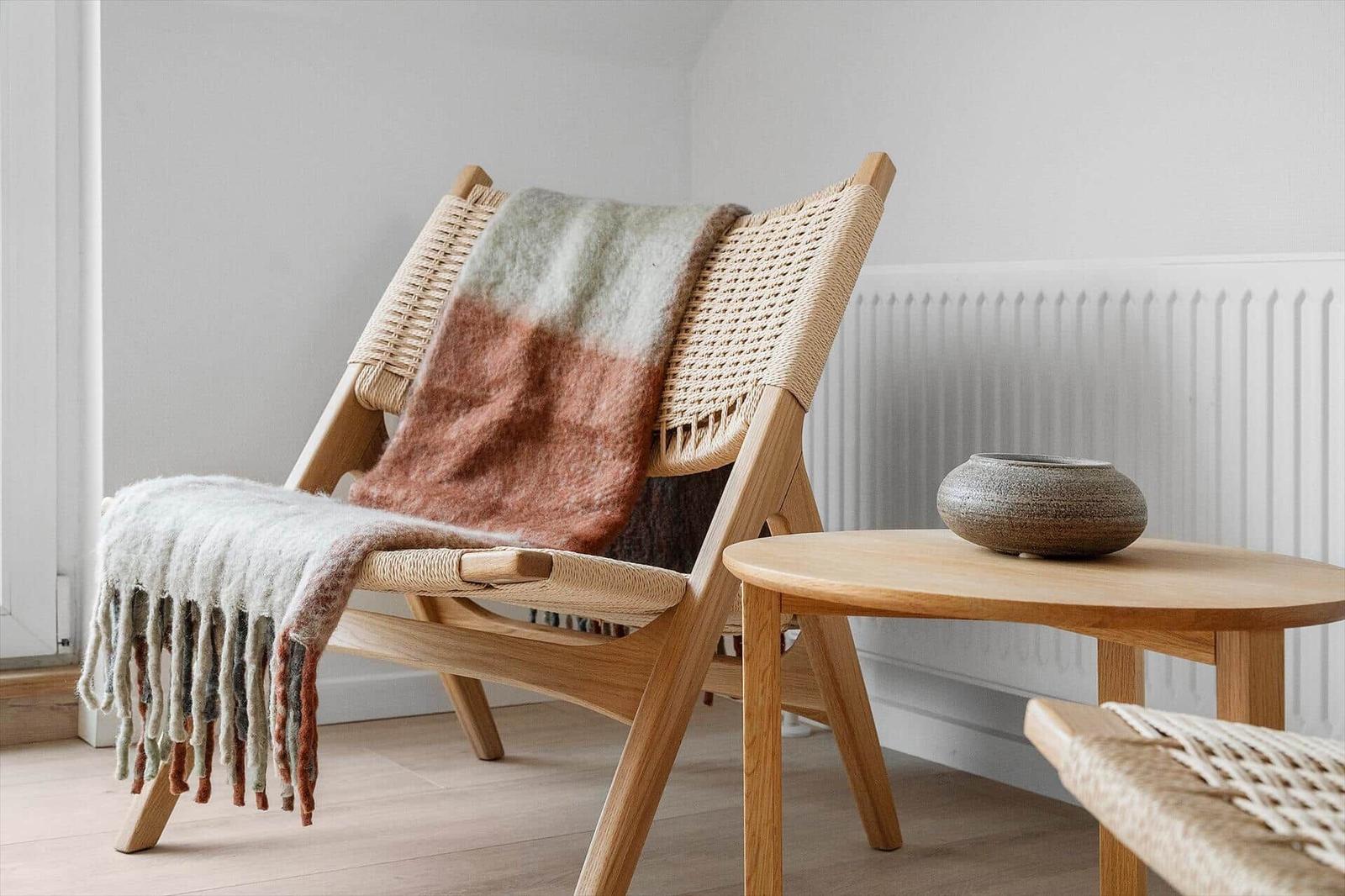 Wooden chair with woven seat and blanket, beside round table with bowl.