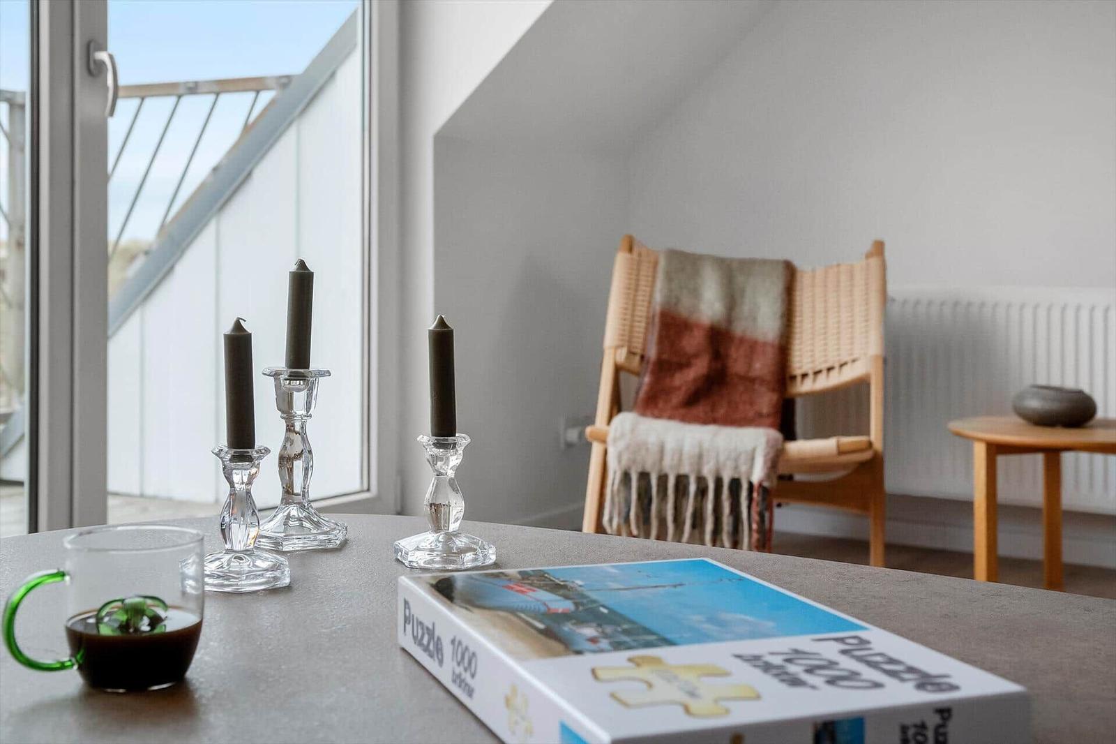 Table with puzzle, mugs, and candle holders near window with balcony view.