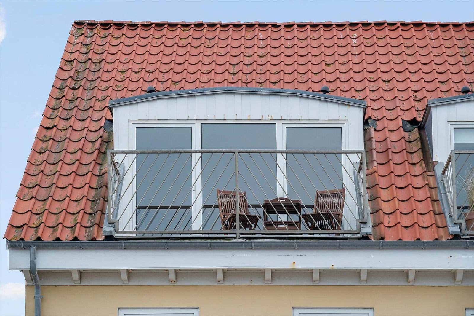 Roof terrace with table and two chairs under red tiled roof.