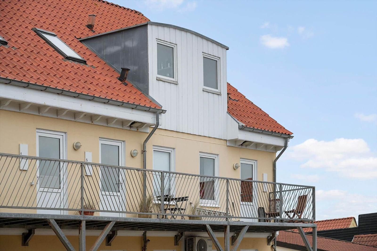 Apartment with balcony, red roof, and white windows under blue sky.