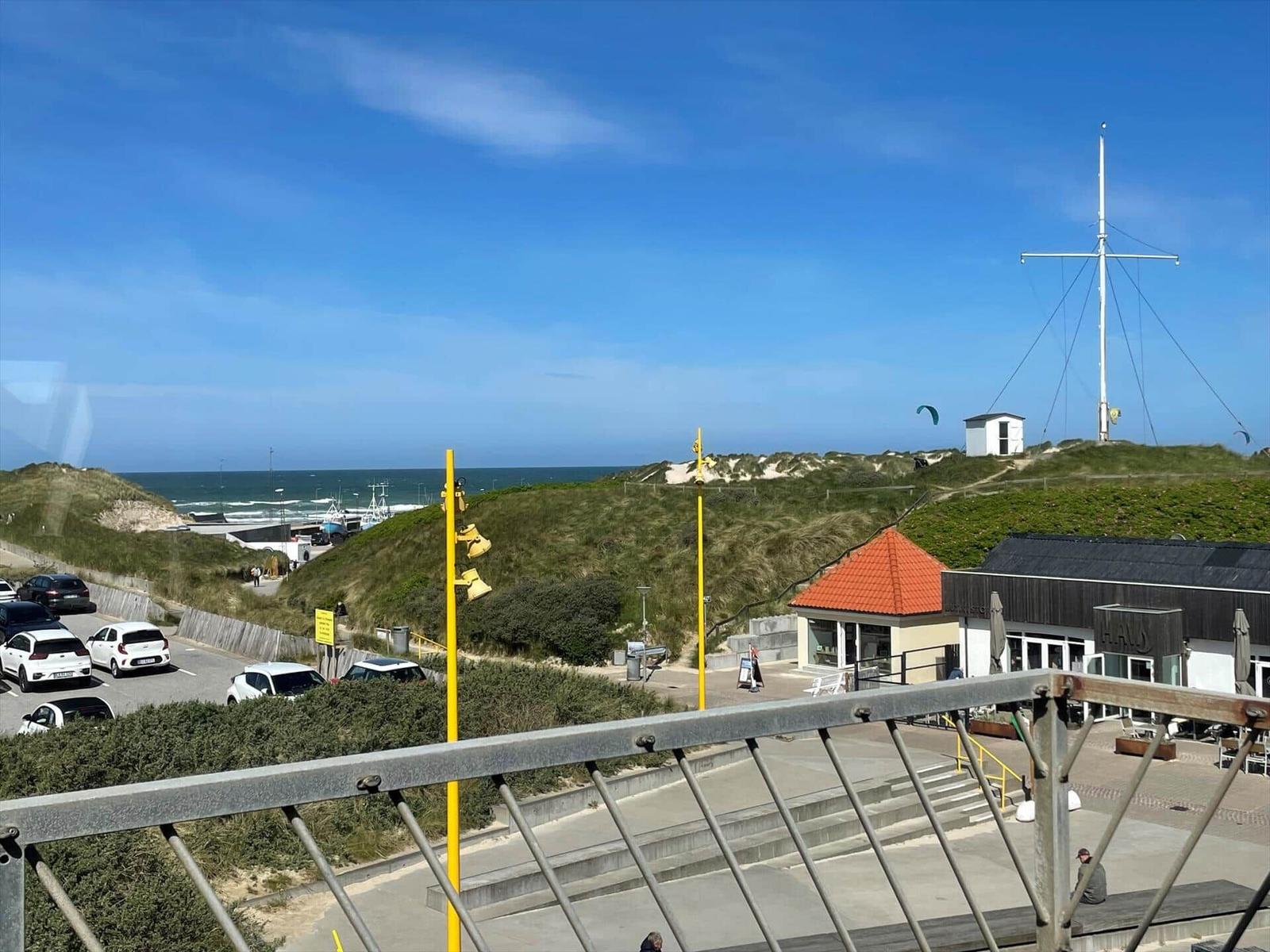 Sea, dunes, and a sailboat on a hill overlooking a beach.