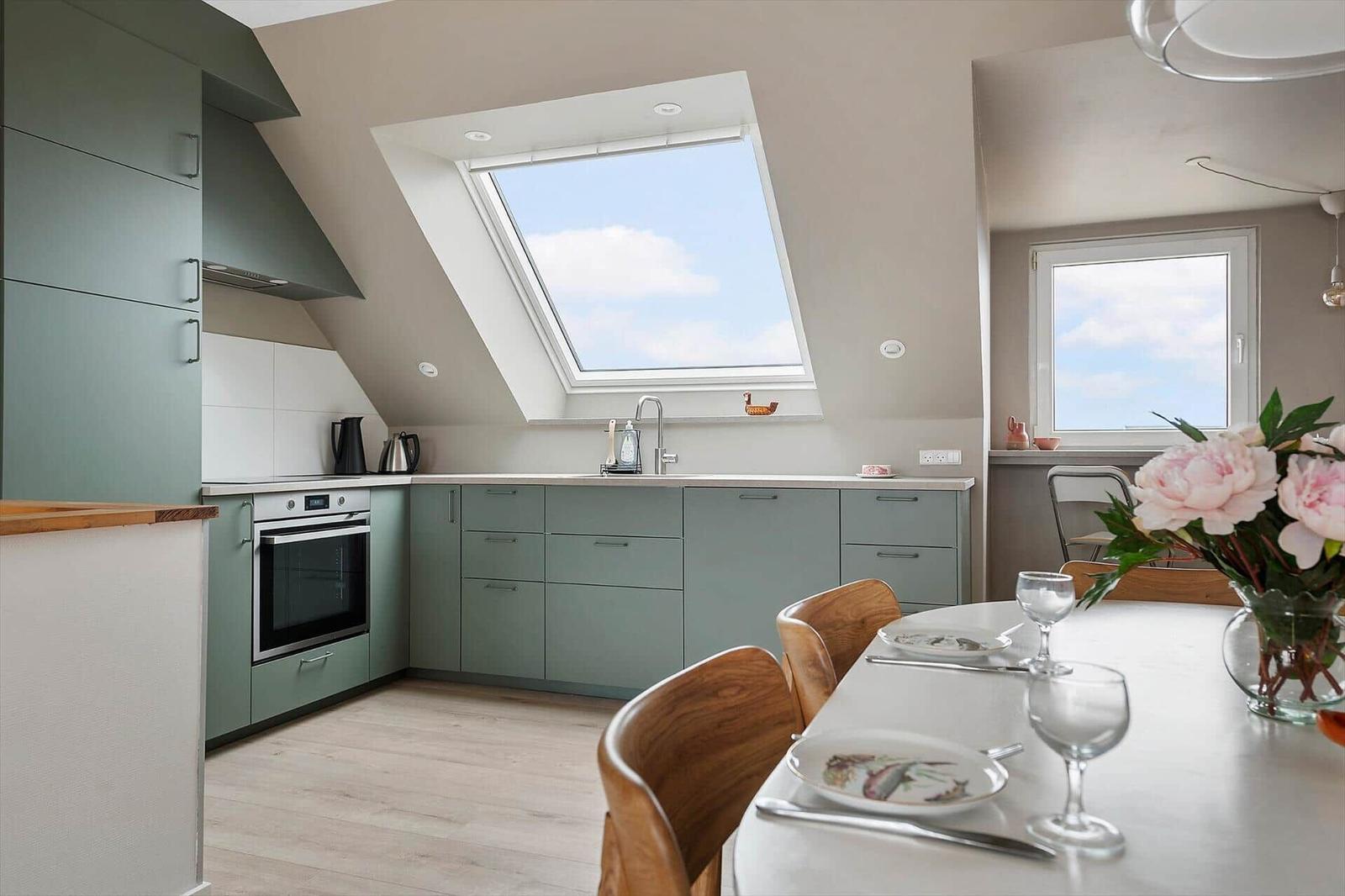 Kitchen with dining area, sloped ceiling, and windows. Wooden chairs and table with flowers.