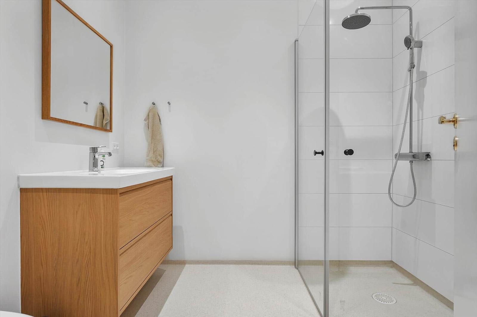 Bathroom with shower, sink, and mirror. Wooden vanity and white tiles.