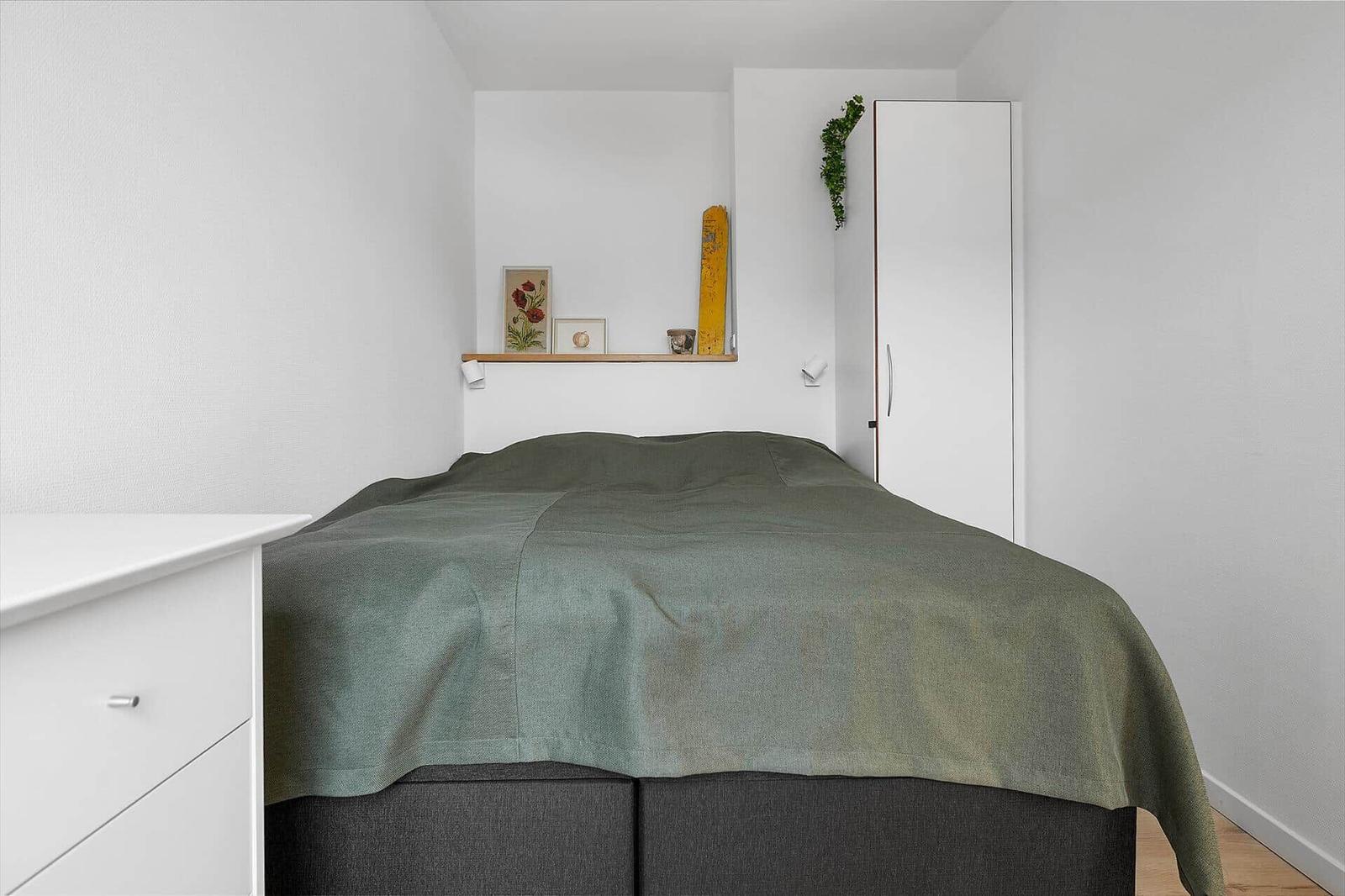 Bedroom with bed, wardrobe, and wall shelf with decorative items.