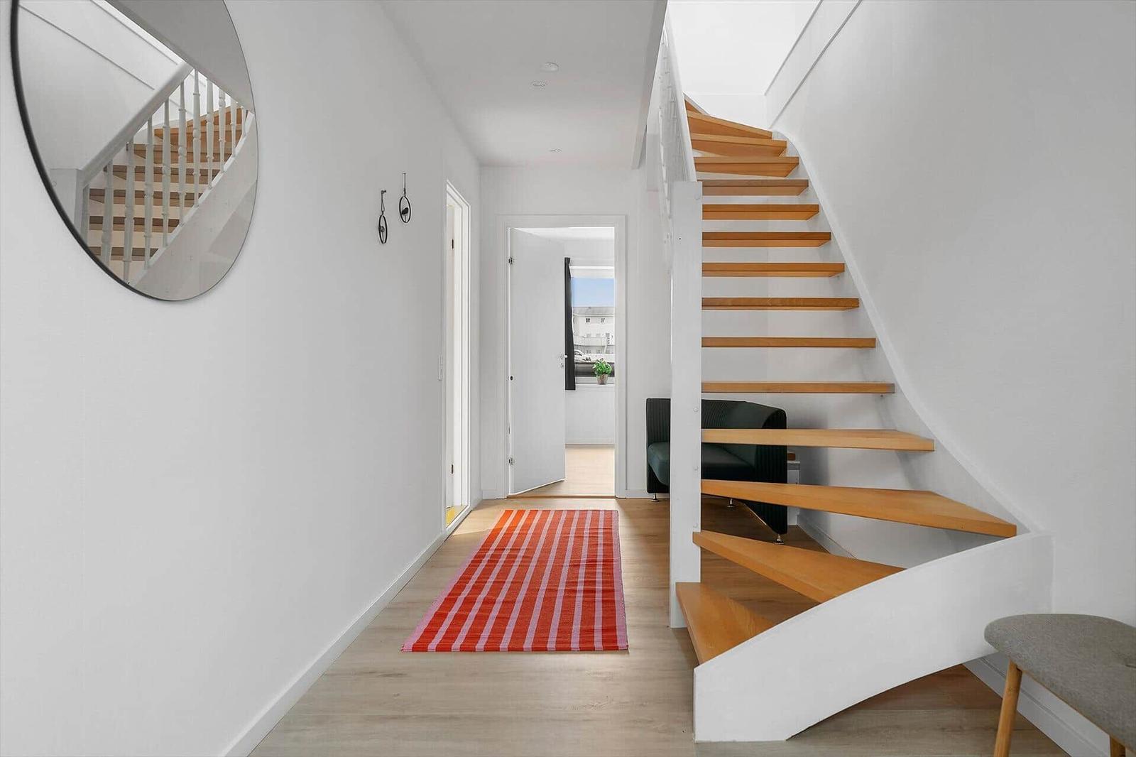 Hallway with wooden staircase, mirror, and rug
