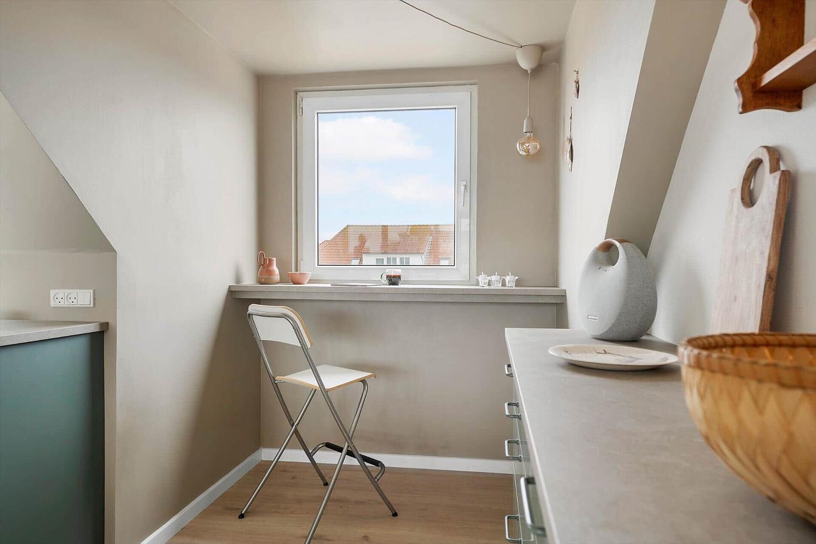 Kitchen with window, chair, and work surface. Roofs are visible outside.