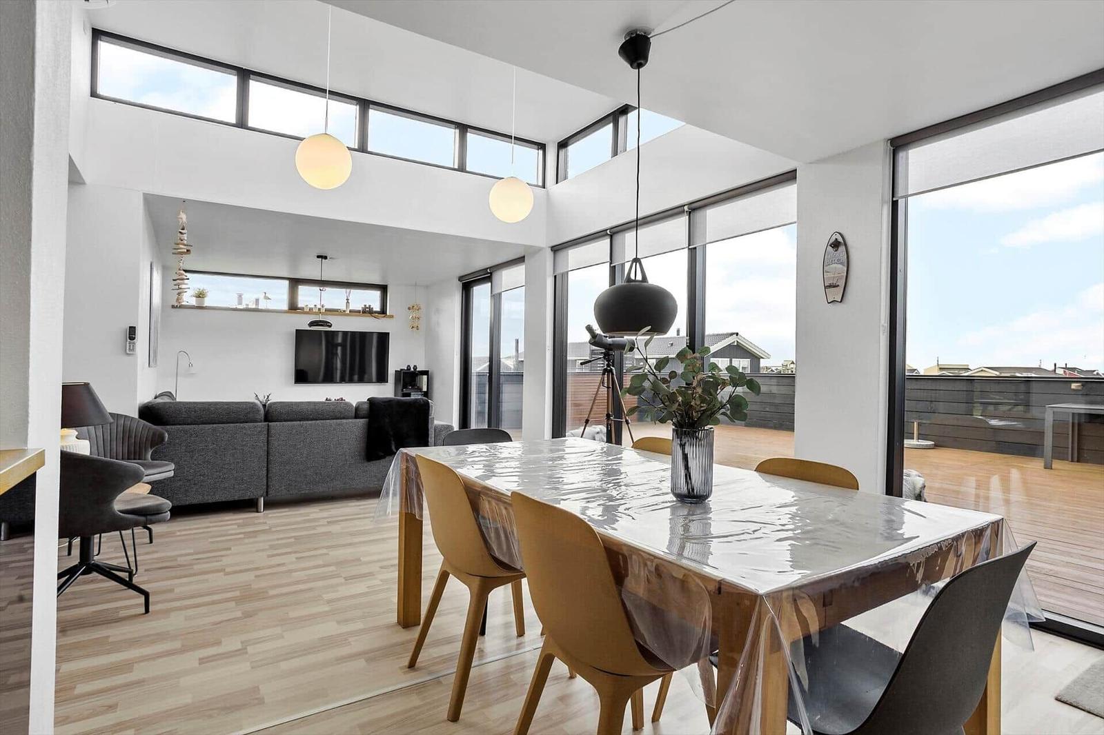 Dining area with table and chairs, living room with sofa and TV, large windows and terrace.