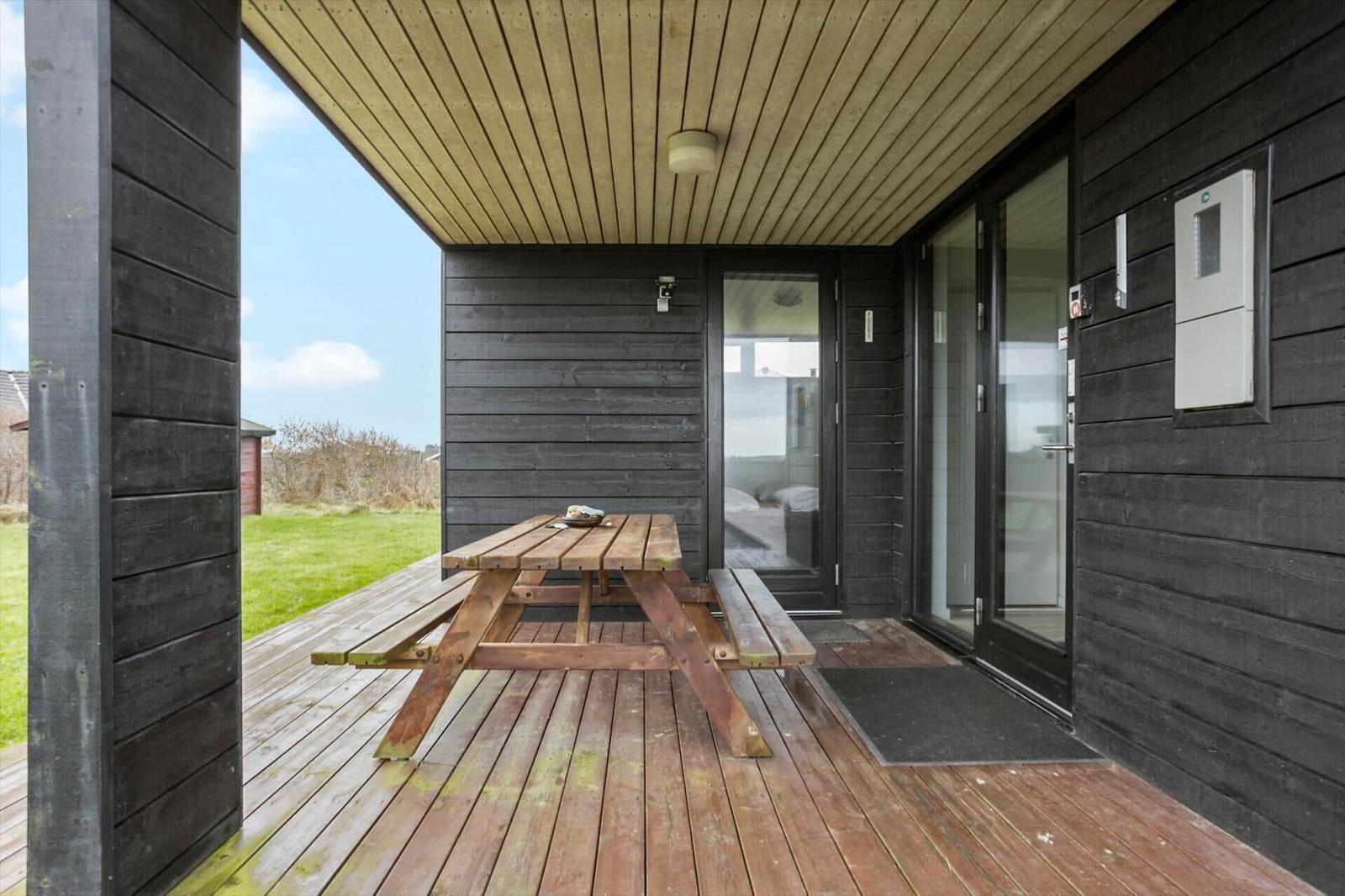 Deck with wooden table and benches, view of grass and sky.