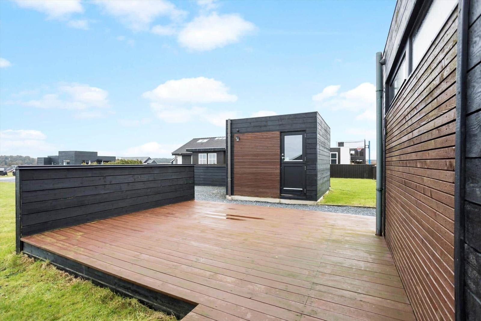 Deck with wooden floor and fence. Background: modern houses and green area.