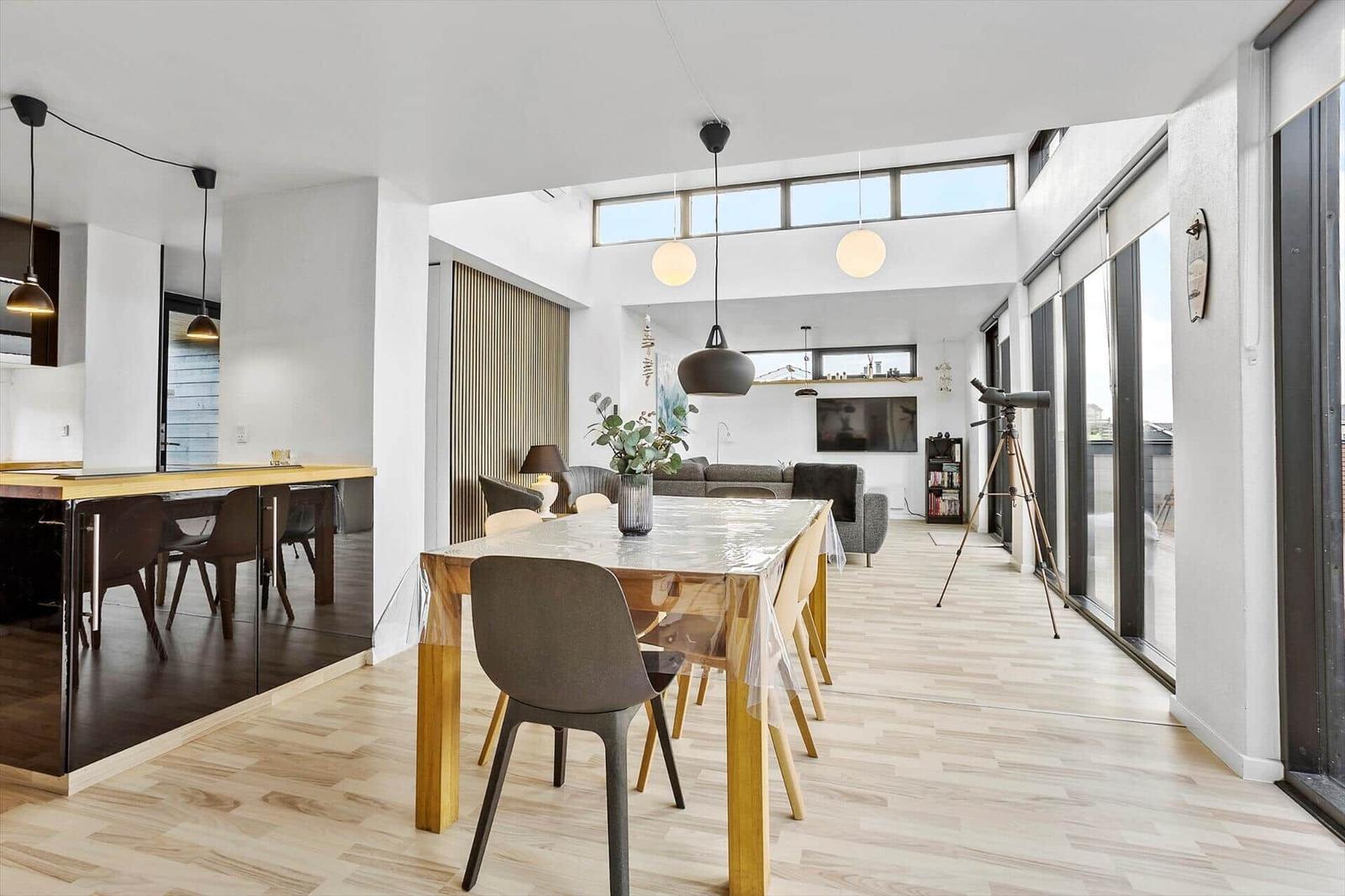 Dining area with table and chairs, living area with sofa and TV, large windows and telescope.