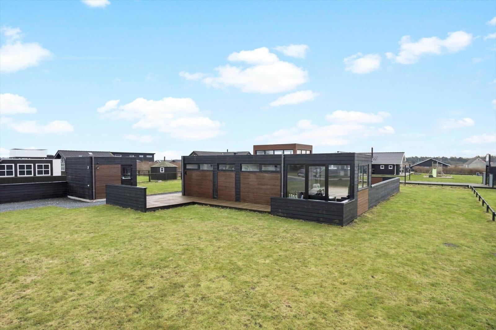 Modern wooden cabin with large garden and terrace under blue sky.