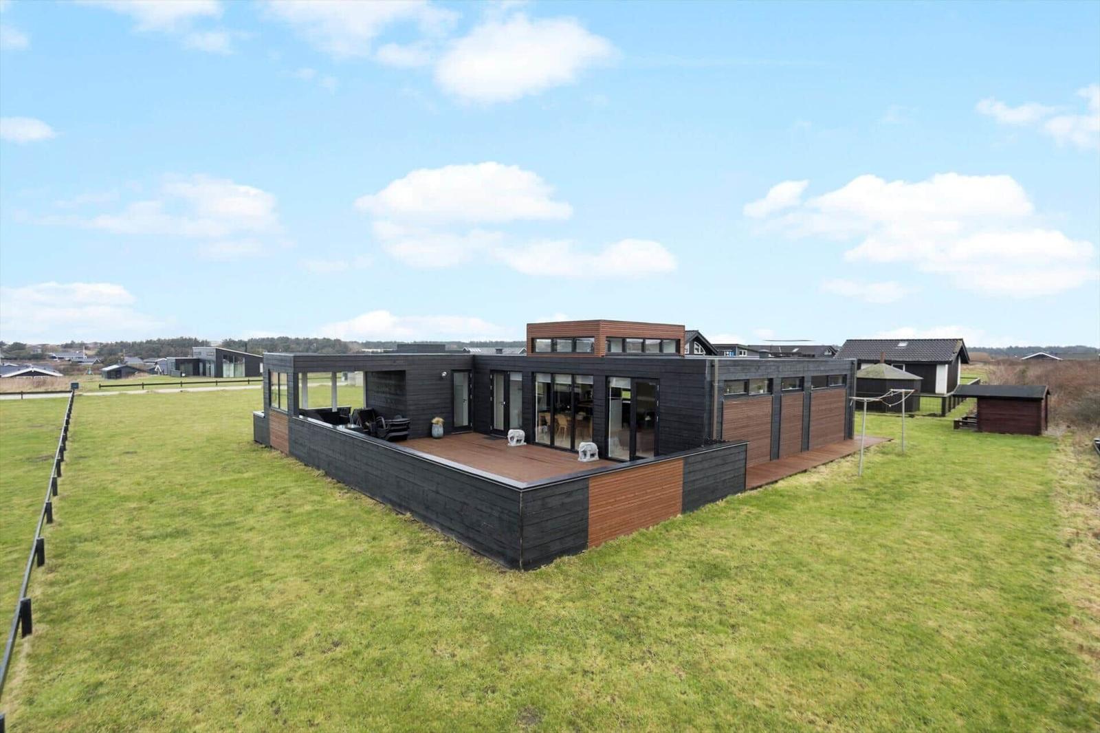 Modern villa with wooden terrace and large garden. View of neighboring houses.